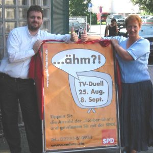 Gabi Frechen und Guido van den Berg präsentieren das Ähm-Plakat.