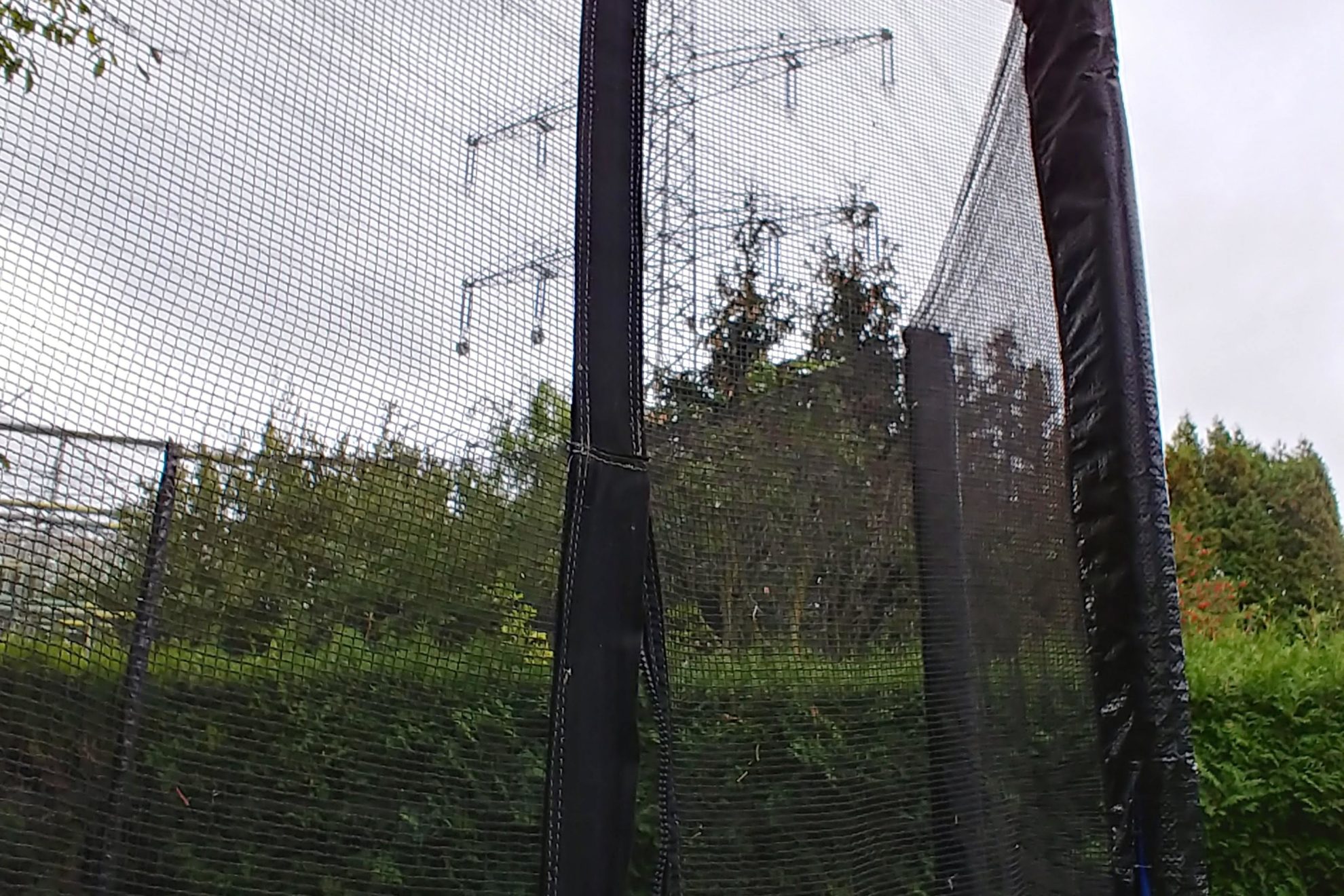 Blick aus einem Garten zur driekt daneben verlaufenden Ultranetleitung durch das Netz eines Trampolins