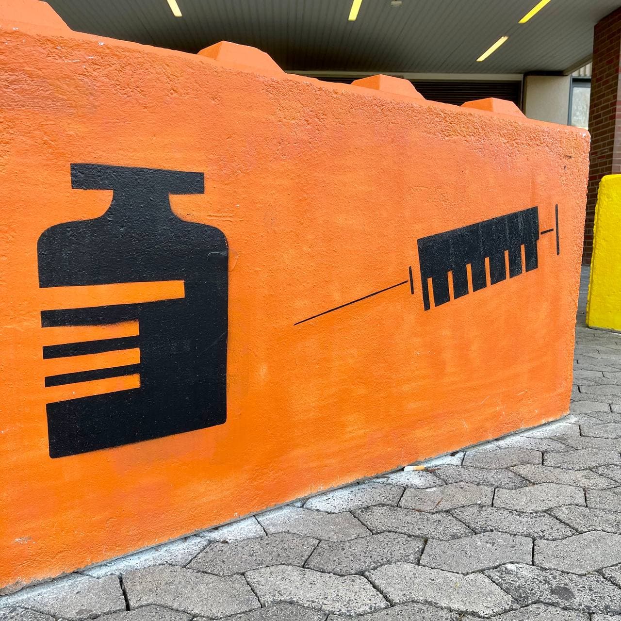 Impfzentrum Hürth Darstellung Spritze und Viole auf Betonblock vor Gebäude