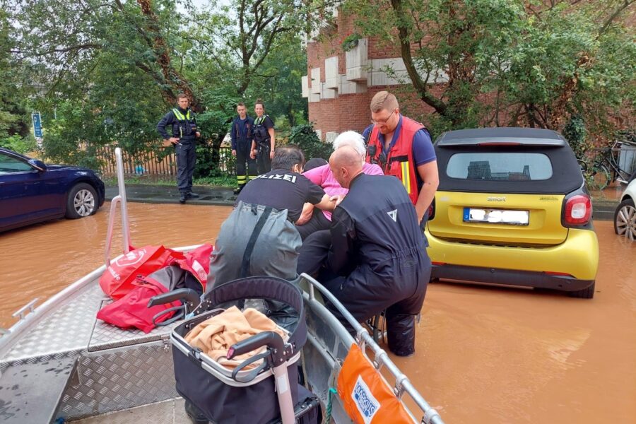 Fluthelfer von DLRG und Feuerwehr heben eine ältere Dame in ein Rettungsboot in einer überfluteten Straße
