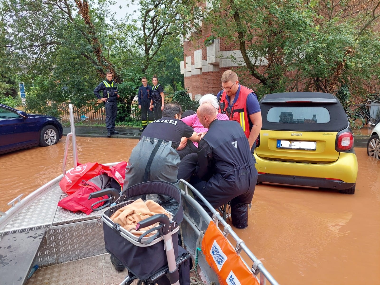 Fluthelfer von DLRG und Feuerwehr heben eine ältere Dame in ein Rettungsboot in einer überfluteten Straße